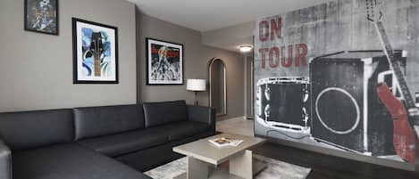 A modern living room with a black leather sofa, a coffee table, framed artwork on the walls, and a large poster on the wall.