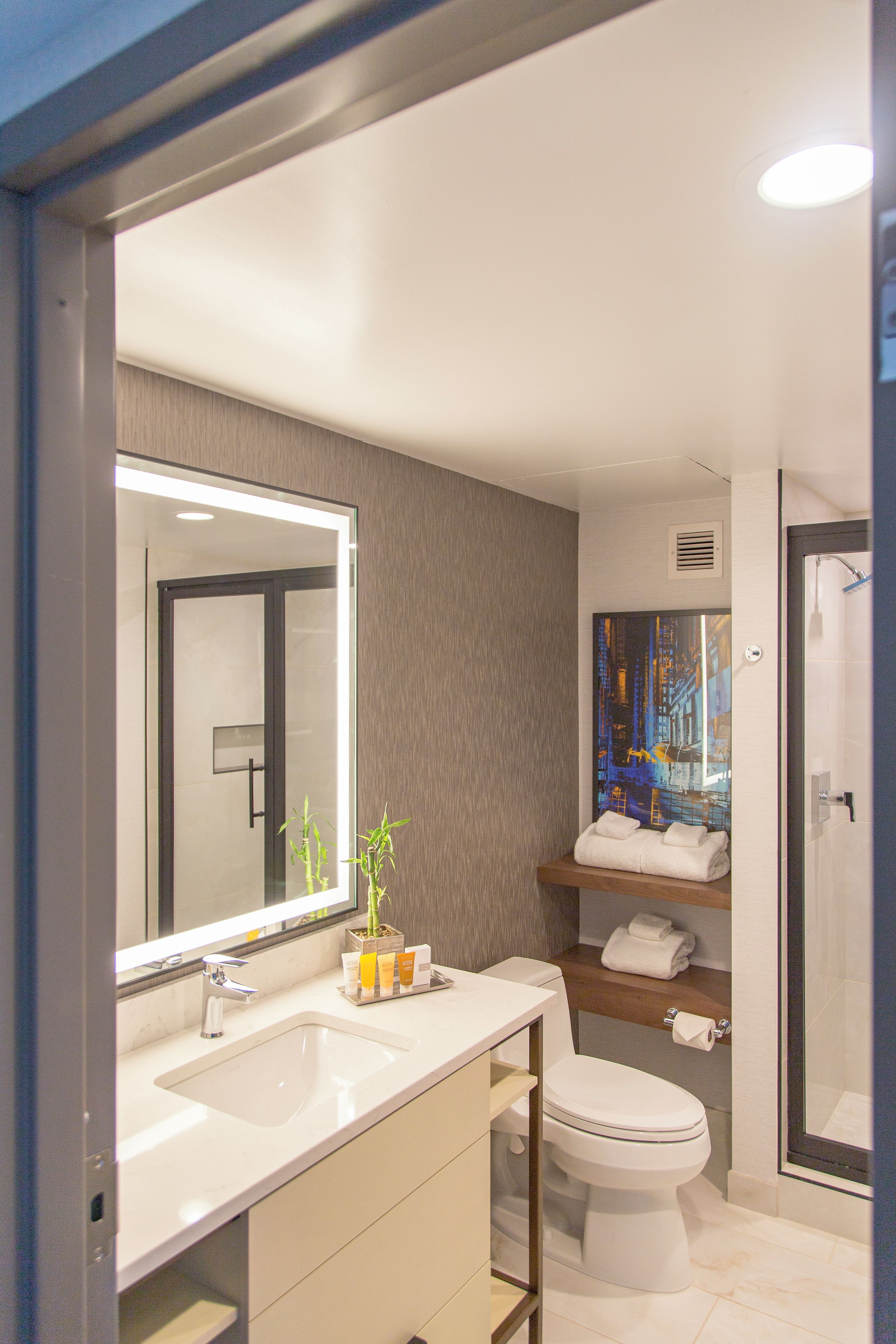 A modern bathroom with a large mirror, a sink, a toilet, and a shower area.