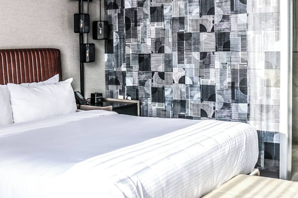 Ein modernes Hotelzimmer mit einem großen Bett, einem Nachttisch, einem an der Wand montierten Telefon und einem gemusterten Vorhang.