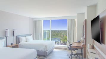 Habitación de hotel con dos camas, un escritorio, un televisor y vistas a la ciudad.