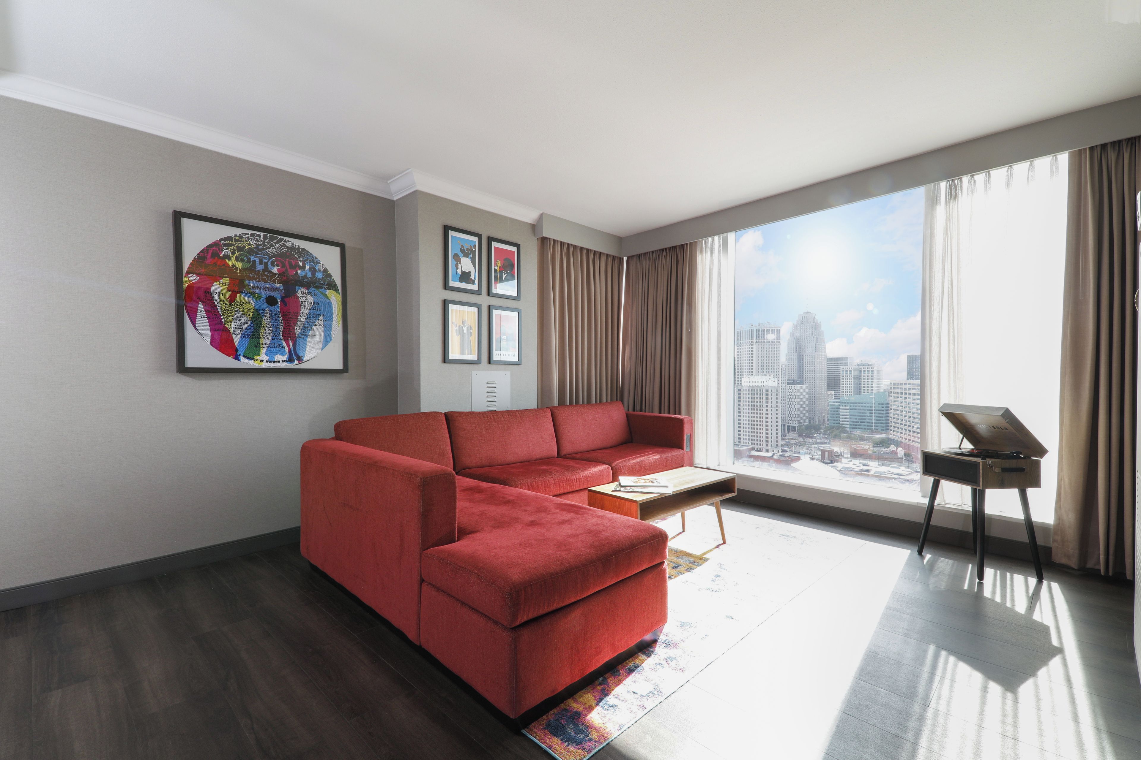 A modern living room with a red sofa, a coffee table, and a city view through large windows.
