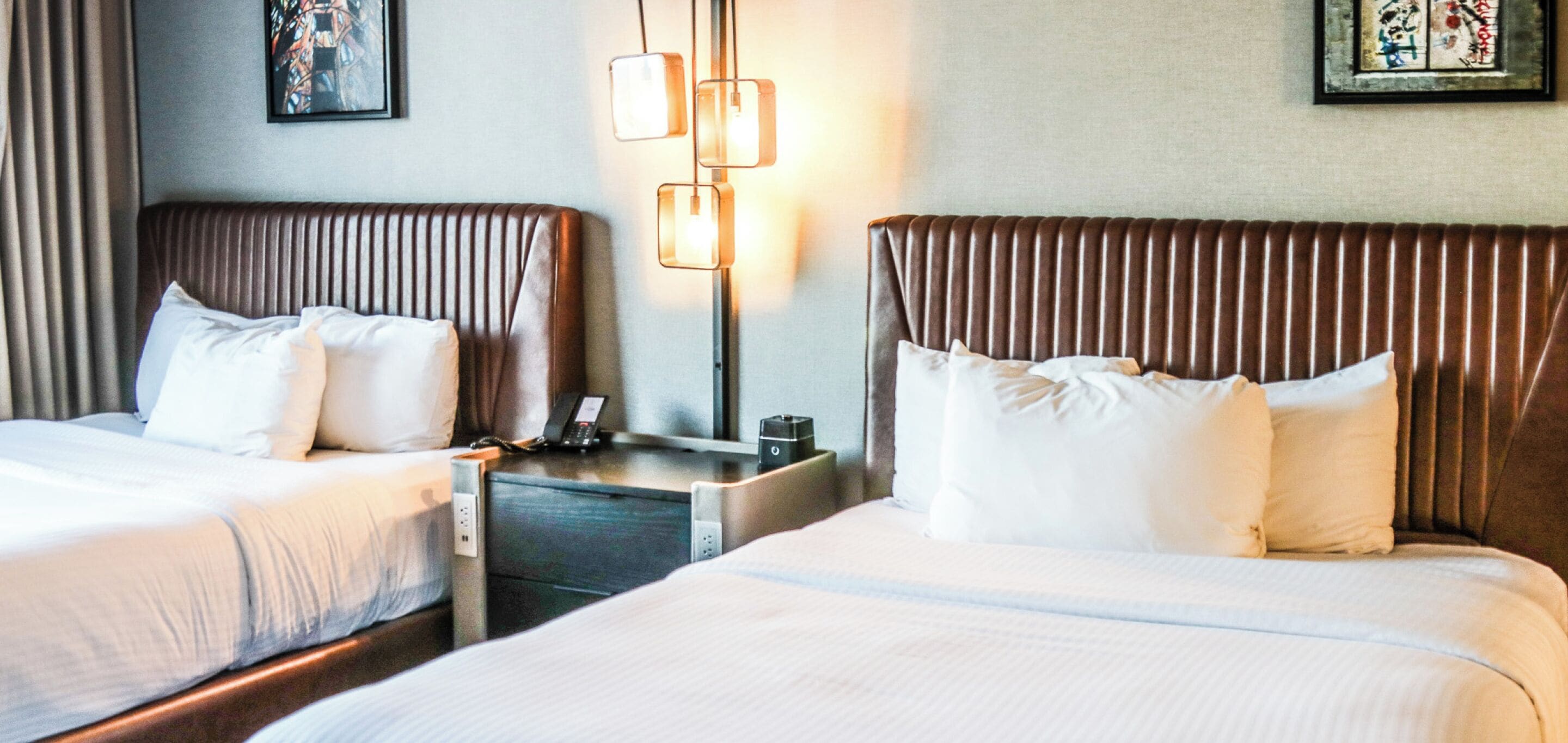 A hotel room with two beds, a bedside table with a phone, and a lamp.