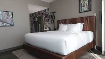 A neatly made bed with white linens, a brown headboard, and a framed abstract painting on the wall.