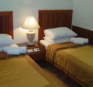 A hotel room with two beds, a nightstand with a lamp, and a wooden headboard. - Chaweng Inn (Koh Samui)