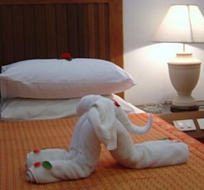 Ein Hotelzimmer mit einem Bett, einem Nachttisch mit Lampe und einer Elefanten-Handtuchskulptur.