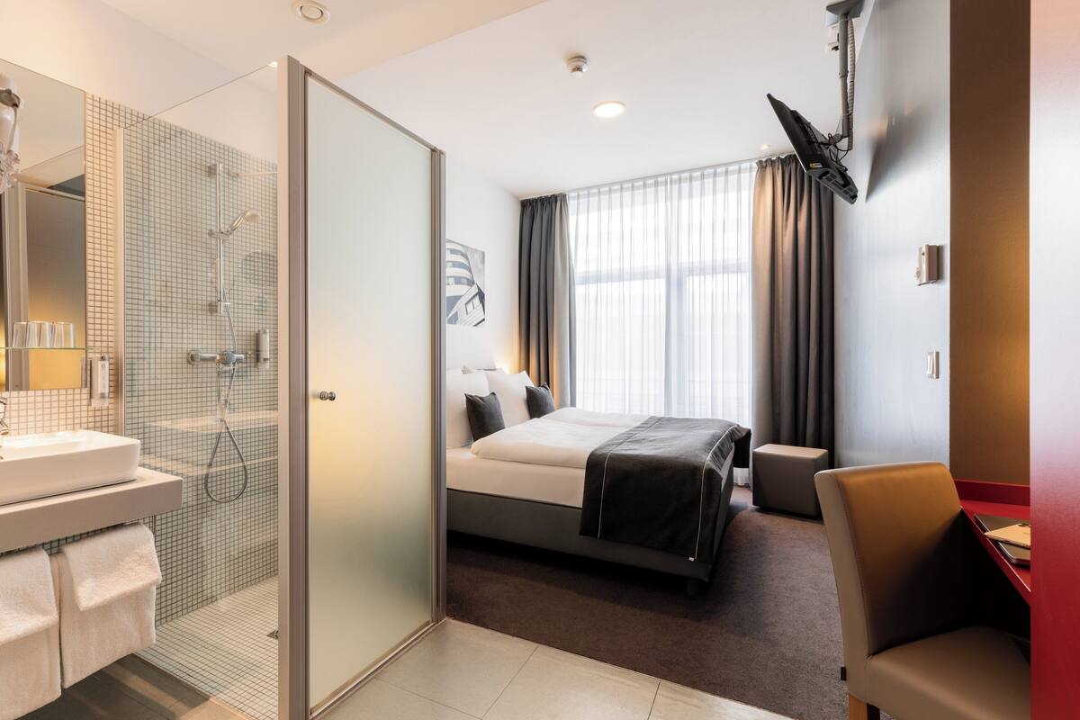 Una habitación de hotel con ducha, cama, escritorio y silla.