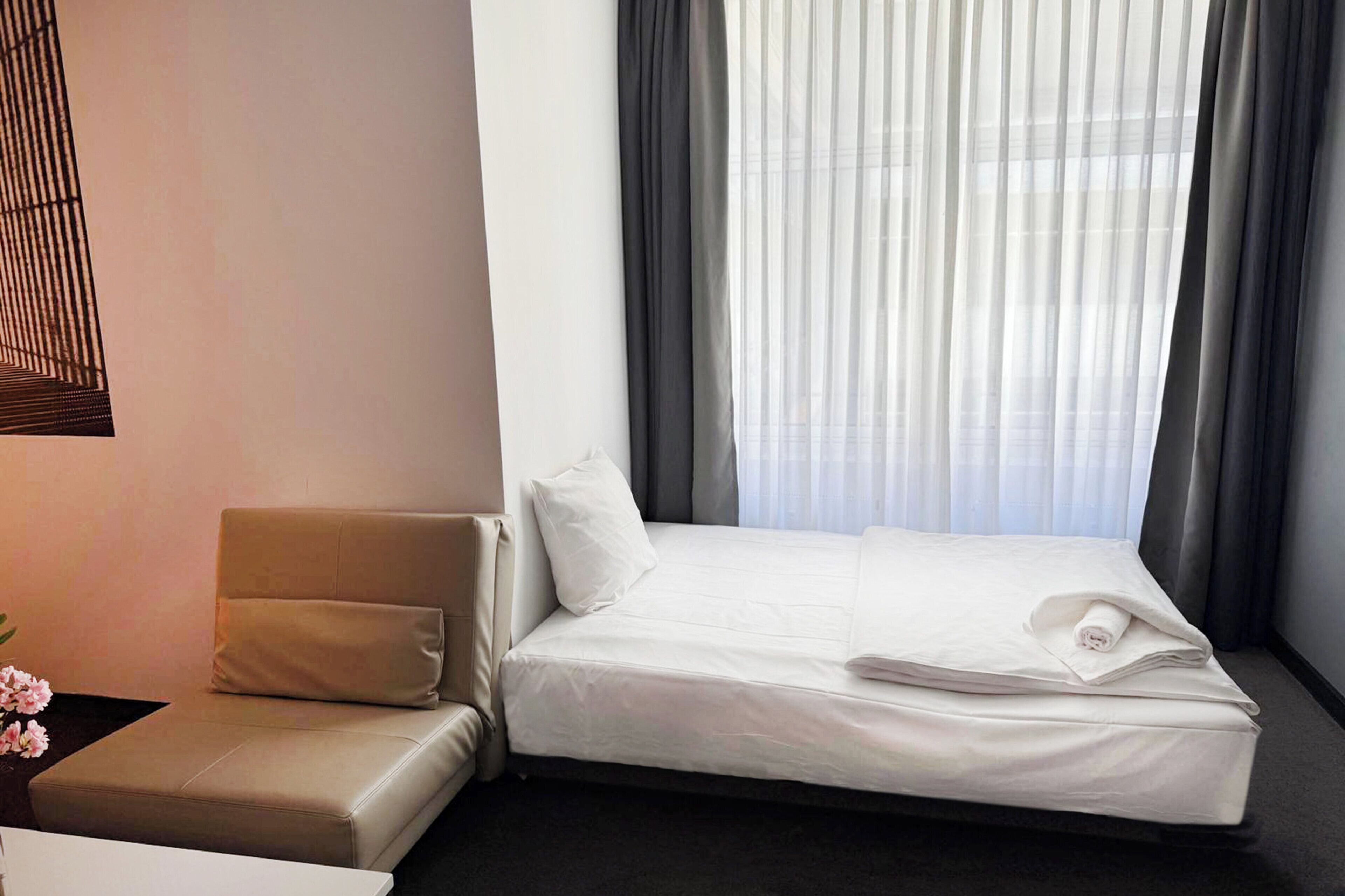 A hotel room with a bed, a sofa, and a window with curtains.