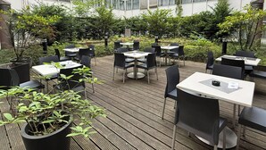 An outdoor dining area with tables and chairs, surrounded by greenery and a building in the background. - Garner Hotel Berlin - Gendarmenmarkt by IHG (Berlin)