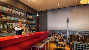A bar area with a cityscape mural, bar stools, and a bartender. - Garner Hotel Berlin - Gendarmenmarkt by IHG (Berlin)