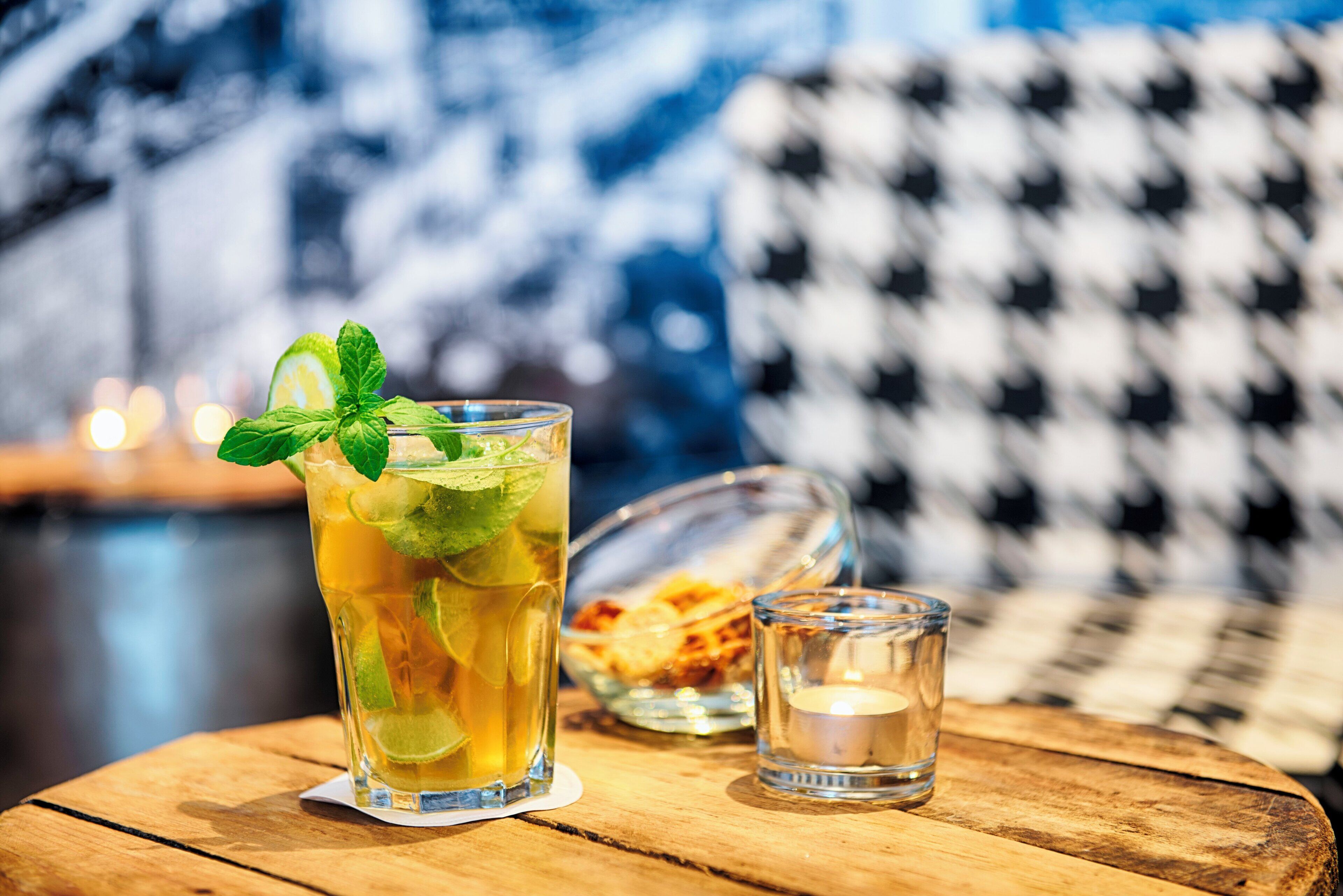 A glass of iced tea with mint on a wooden table, a small glass of water, and a bowl of cookies in the background.
