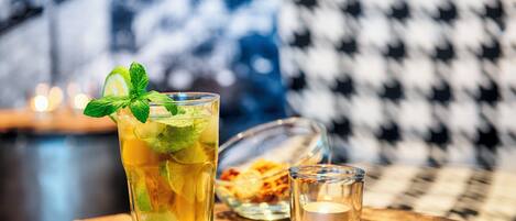 A glass of iced tea with mint on a wooden table, a small glass of water, and a bowl of cookies in the background.