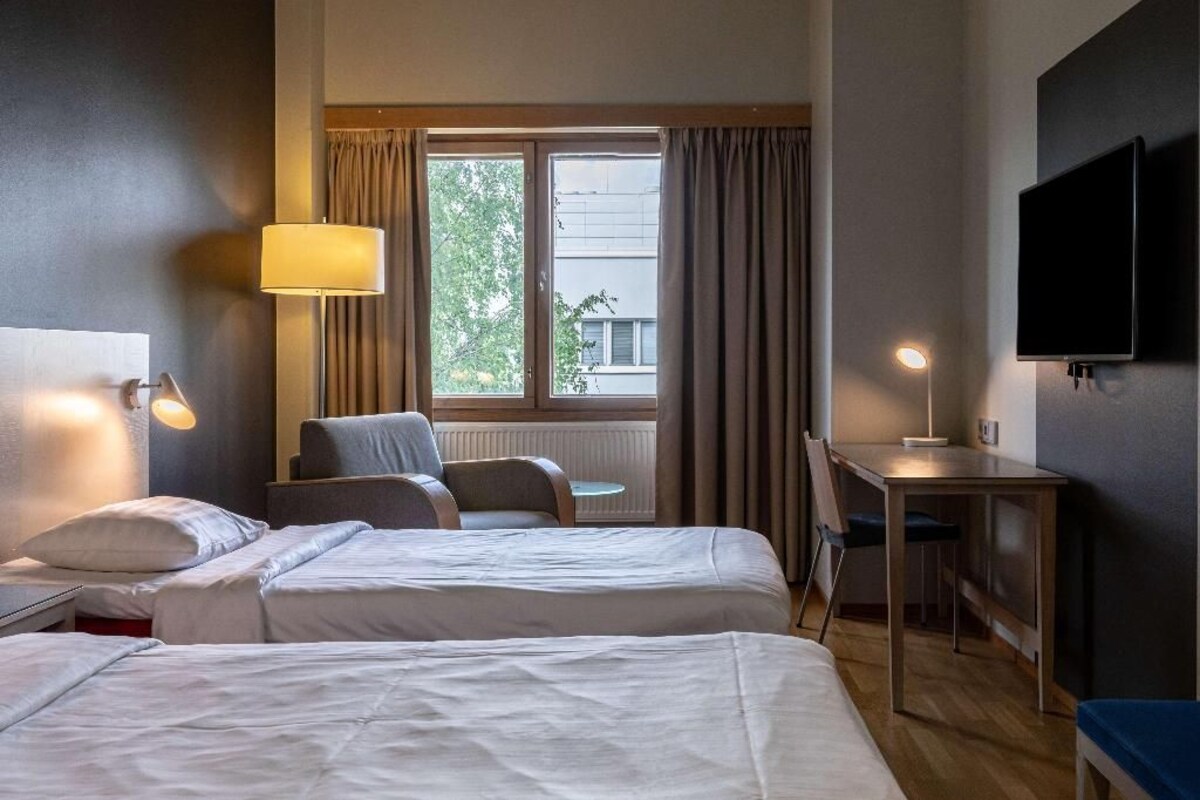 A hotel room with two beds, a desk, a chair, a TV, and a window with curtains.