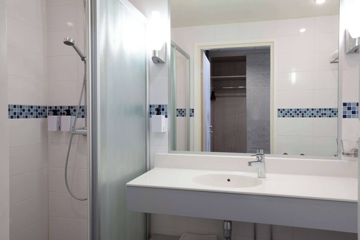 Une salle de bain moderne avec un lavabo blanc, une douchette à main et une paroi de douche en verre.