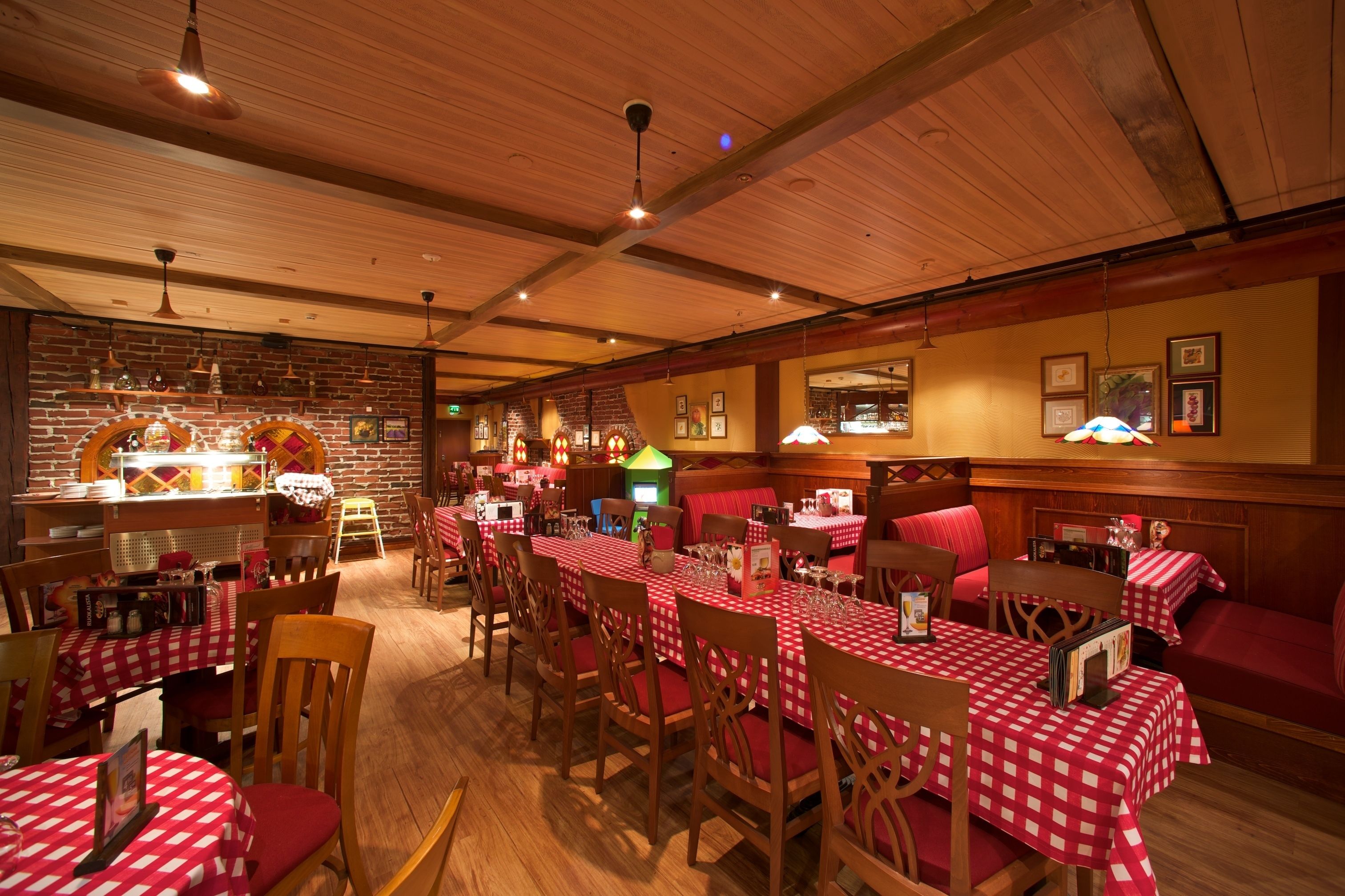 Een restaurant met houten balken in het plafond, rode en witte geruit tafelkleden en bakstenen muren.