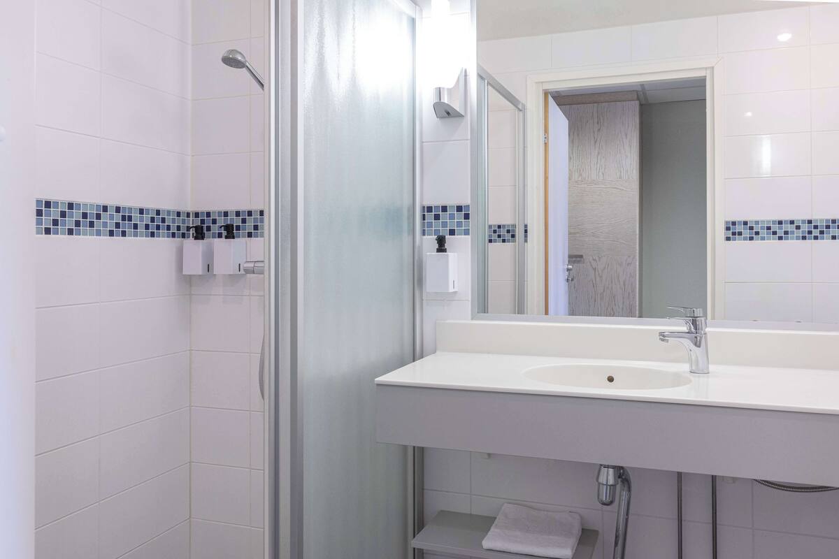 Une salle de bain moderne avec une douche à parois de verre, un lavabo blanc avec un miroir et un porte-serviettes.