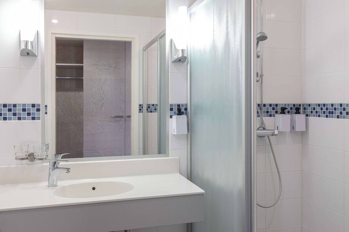 Une salle de bain avec un lavabo blanc, un miroir, une douche et un porte-serviettes.