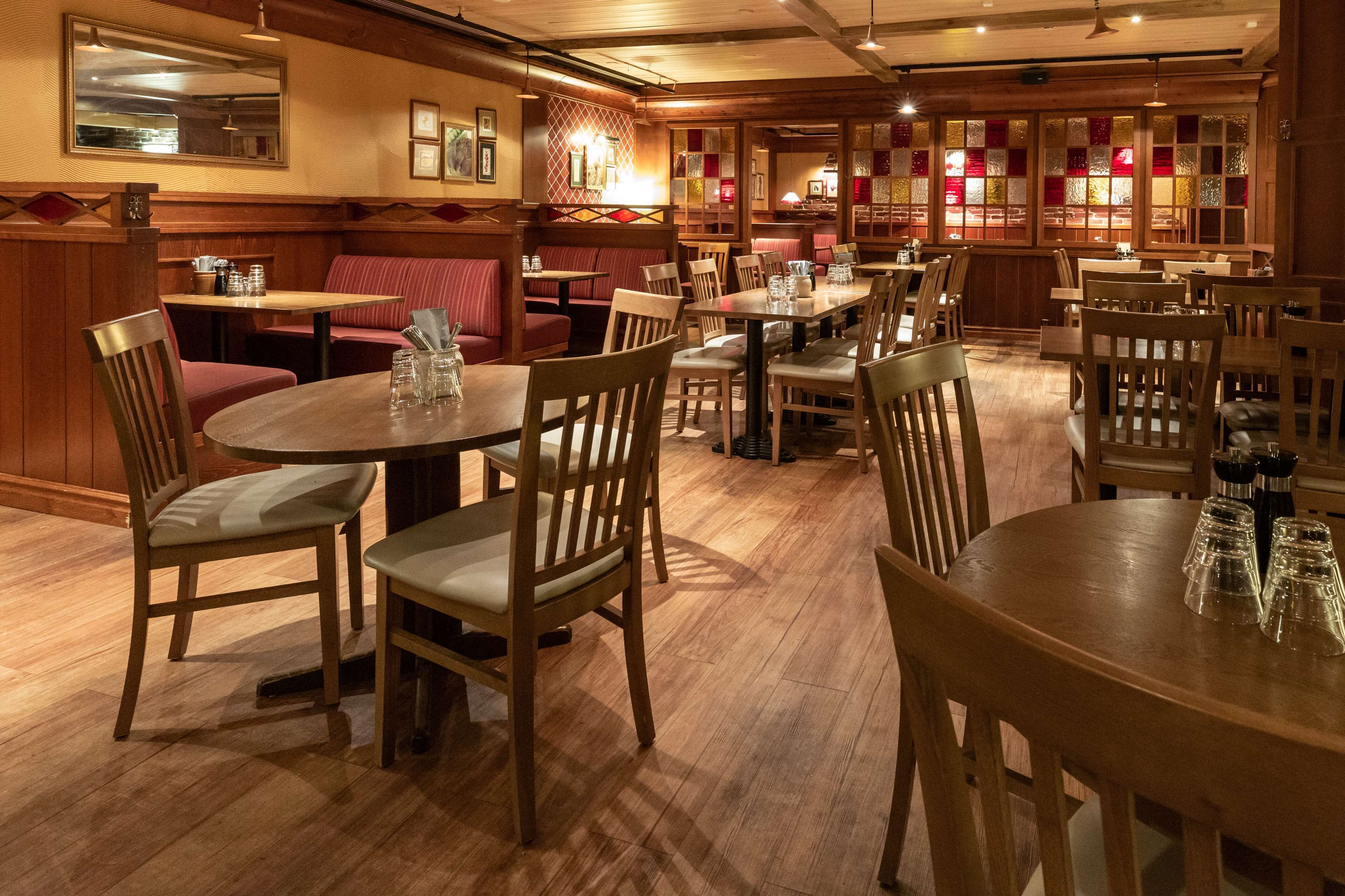 Un restaurante con mesas y asientos tipo banca de madera, suelo de madera e iluminación cálida.