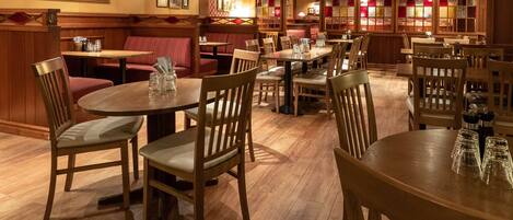 Un restaurante con mesas y asientos tipo banca de madera, suelo de madera e iluminación cálida.