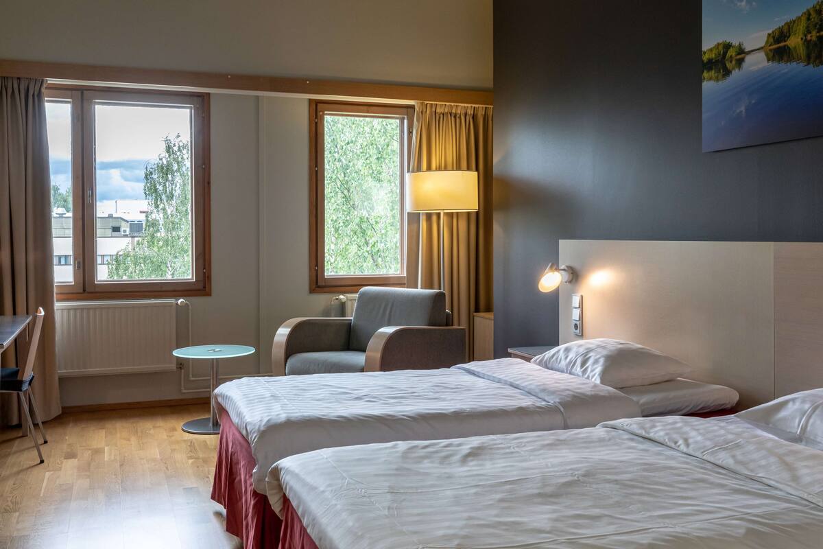 Une chambre d’hôtel avec deux lits, une chaise, une table et une fenêtre avec des rideaux.