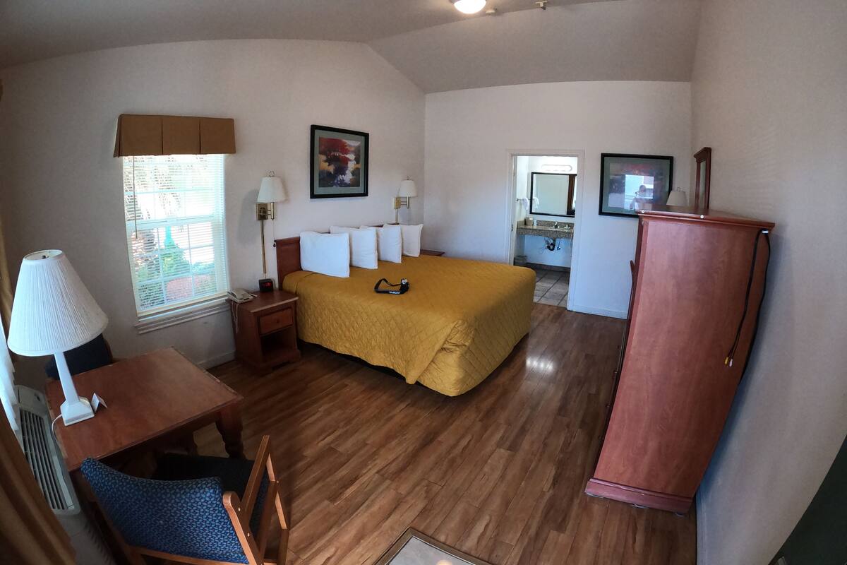 A bedroom with a bed, bedside tables, a desk, a chair, a wardrobe, and a window with blinds.