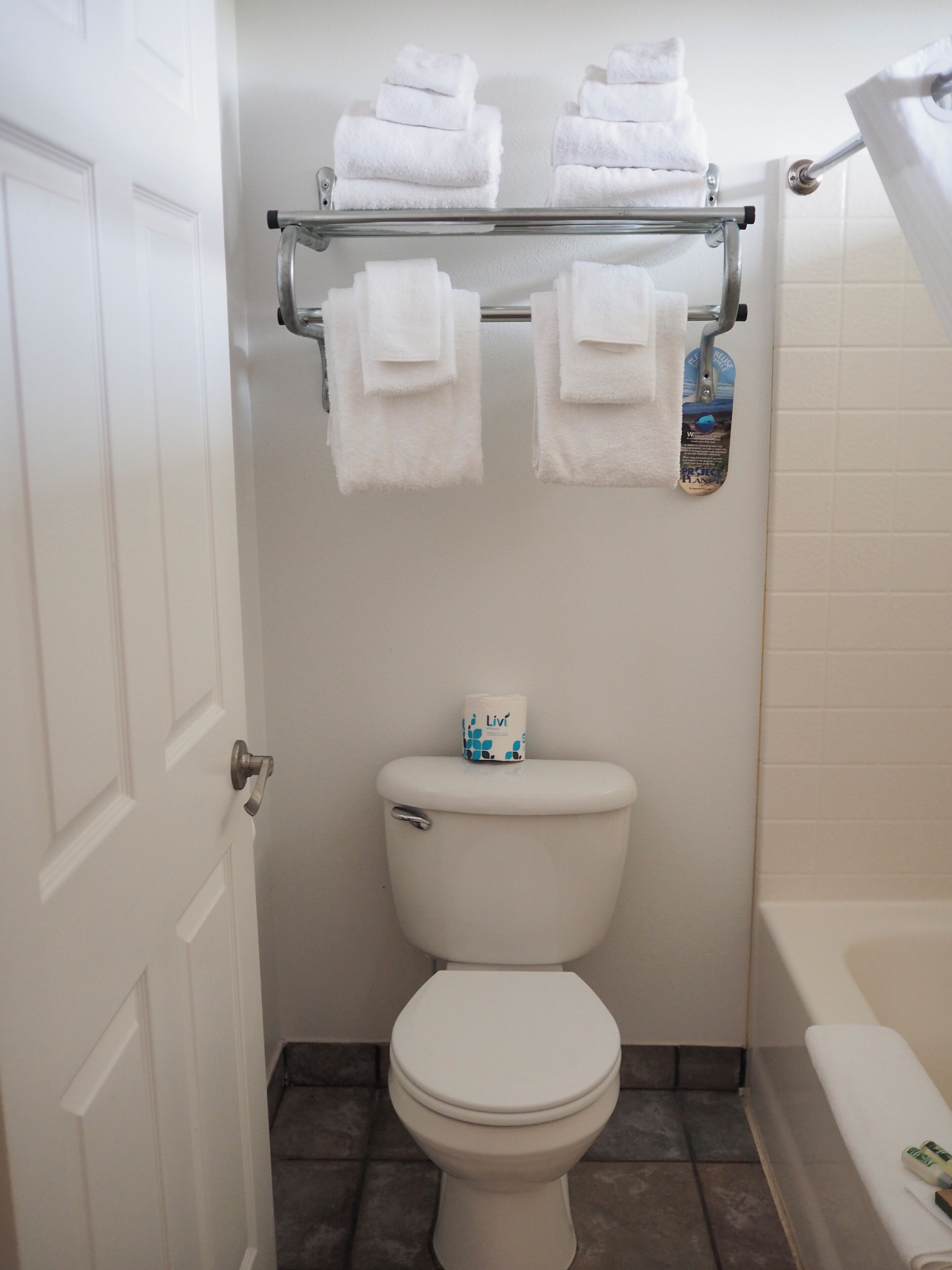 A bathroom with a toilet, a towel rack with folded towels, and a roll of toilet paper.