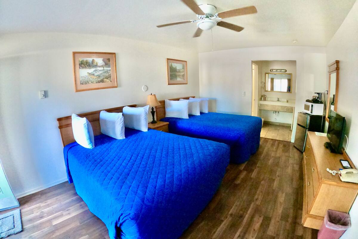 A hotel room with two beds, a ceiling fan, a small desk with a phone, and a bathroom visible through an open door.