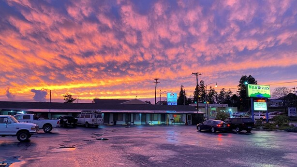 A parking lot with several vehicles, a building with a sign for 'Wild Rivers Motor Lodge', and a sunset sky.