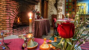 A cozy dining area with a brick fireplace, candles, and a table set for a meal. - Riad Al Madina (Essaouira)