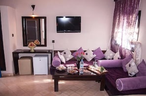 A living room with a sofa, coffee table, TV, and a small fridge.