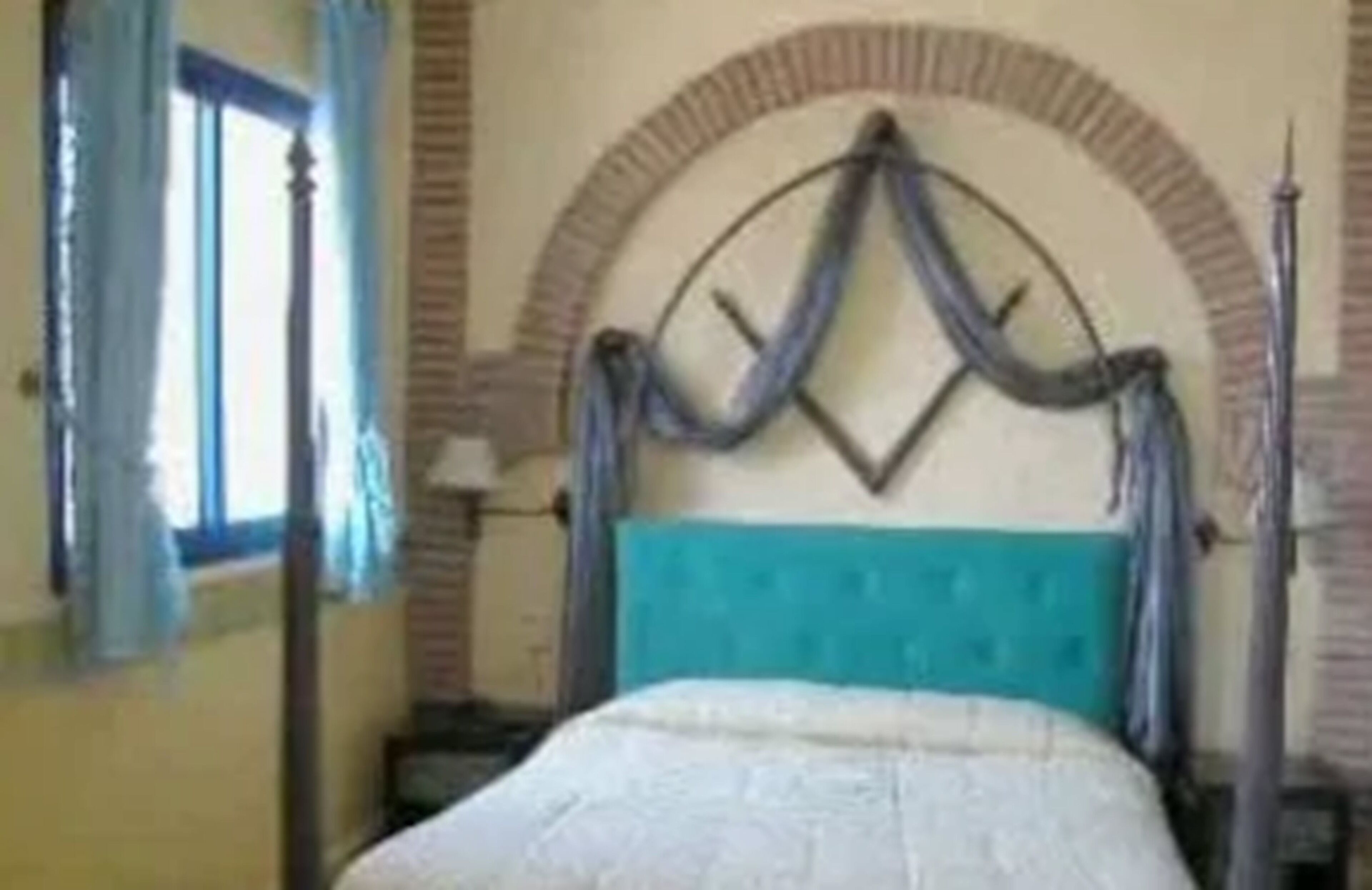 Une chambre avec un lit, une fenêtre avec des rideaux et une arche décorative au-dessus du lit.