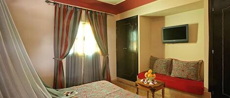 Un dormitorio con una cama, un televisor, un sofá y una mesita con fruta.