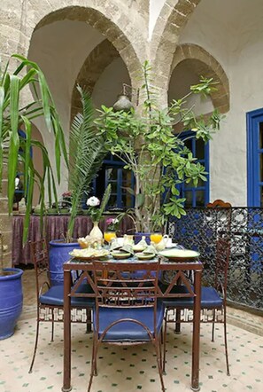 A courtyard with a table set for dining, surrounded by chairs, and potted plants.