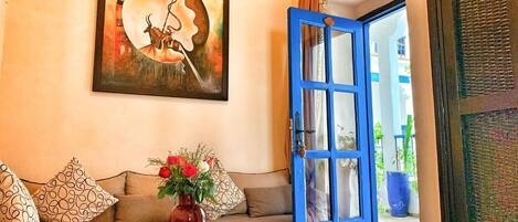 A living room with a sofa, a coffee table with a vase of flowers, a blue door, and a painting on the wall.