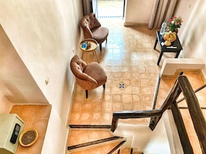 A hotel room with a staircase, two armchairs, a small round table, and a side table with a vase and fruit.