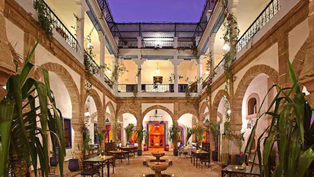 A spacious courtyard with arches, a central fountain, and tables and chairs for dining. - Riad Al Madina (Essaouira)