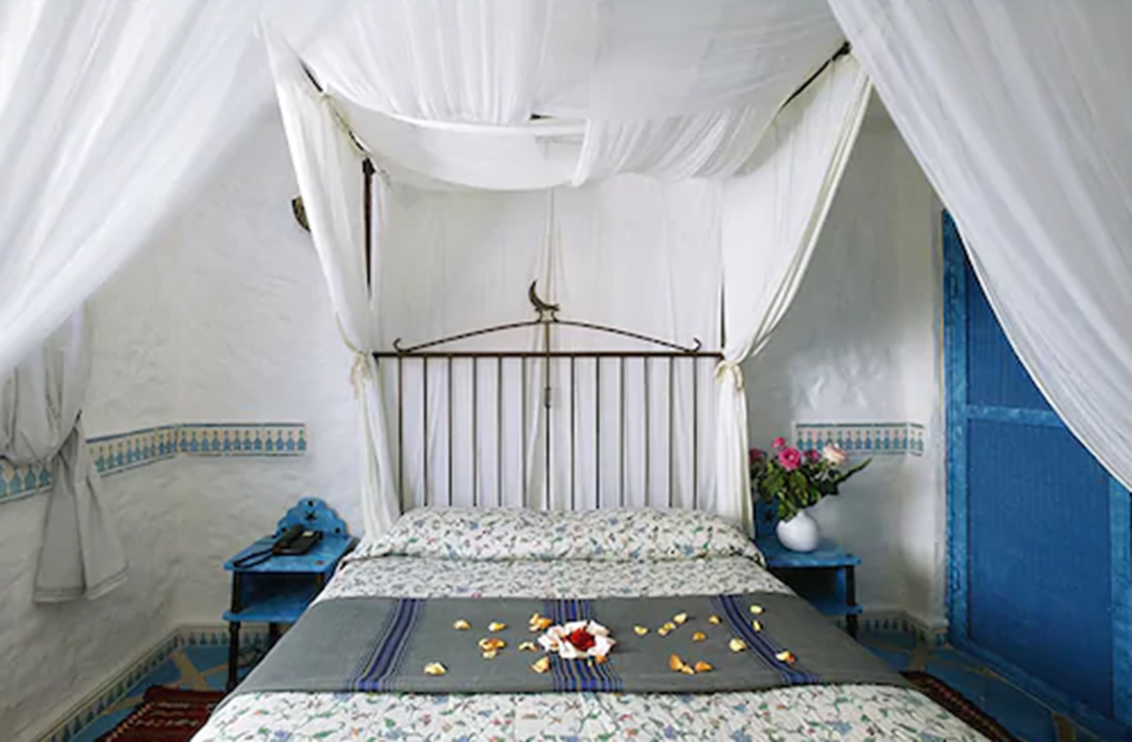 Una habitación con cama, mesita de noche, pared azul y dosel blanco.