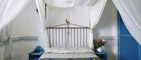 Una habitación con cama, mesita de noche, pared azul y dosel blanco.