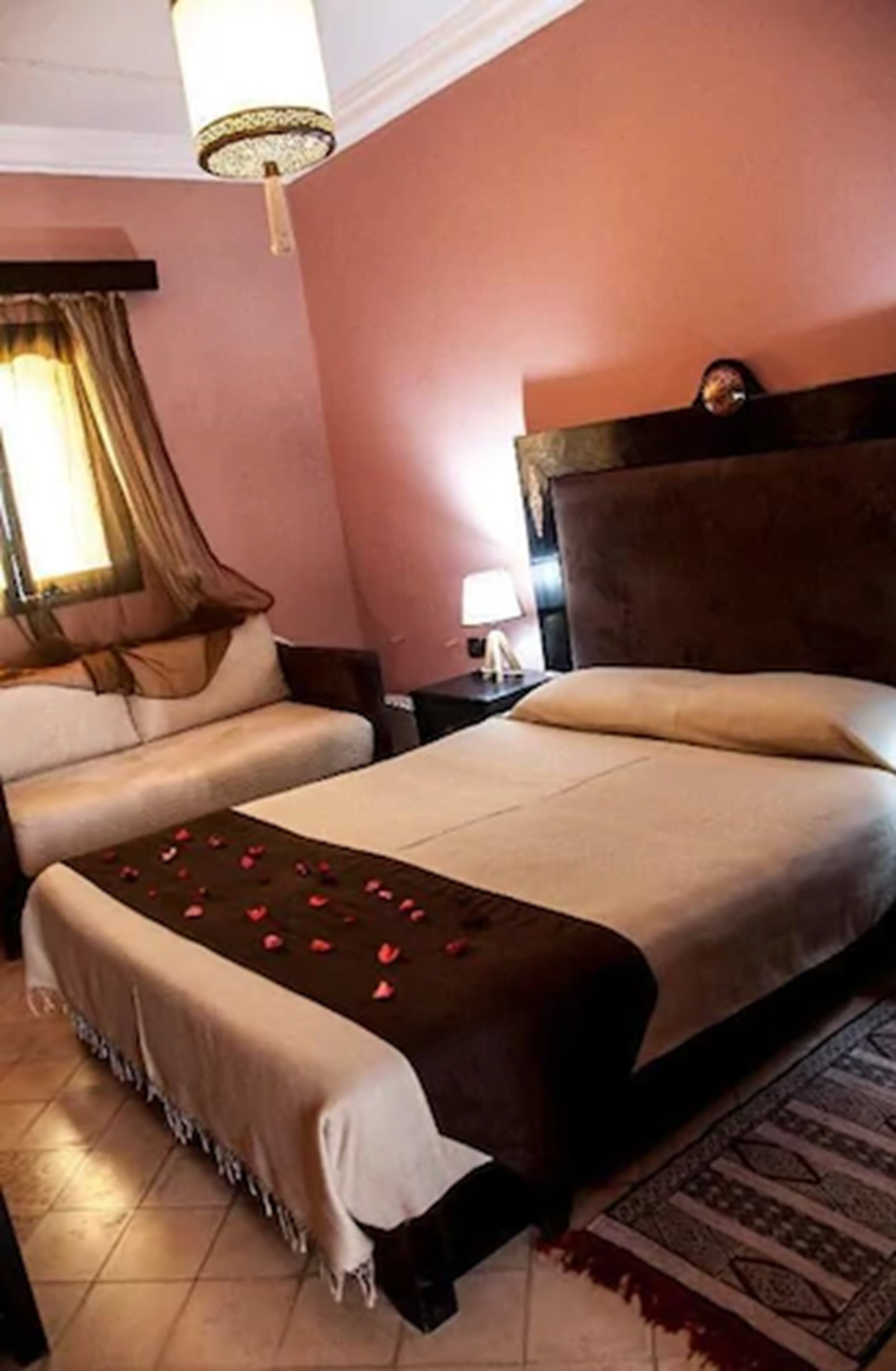 A hotel room with a large bed, a smaller sofa, a nightstand, and a lamp.