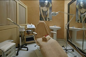 A medical examination room with a patient bed, examination table, and two sinks.