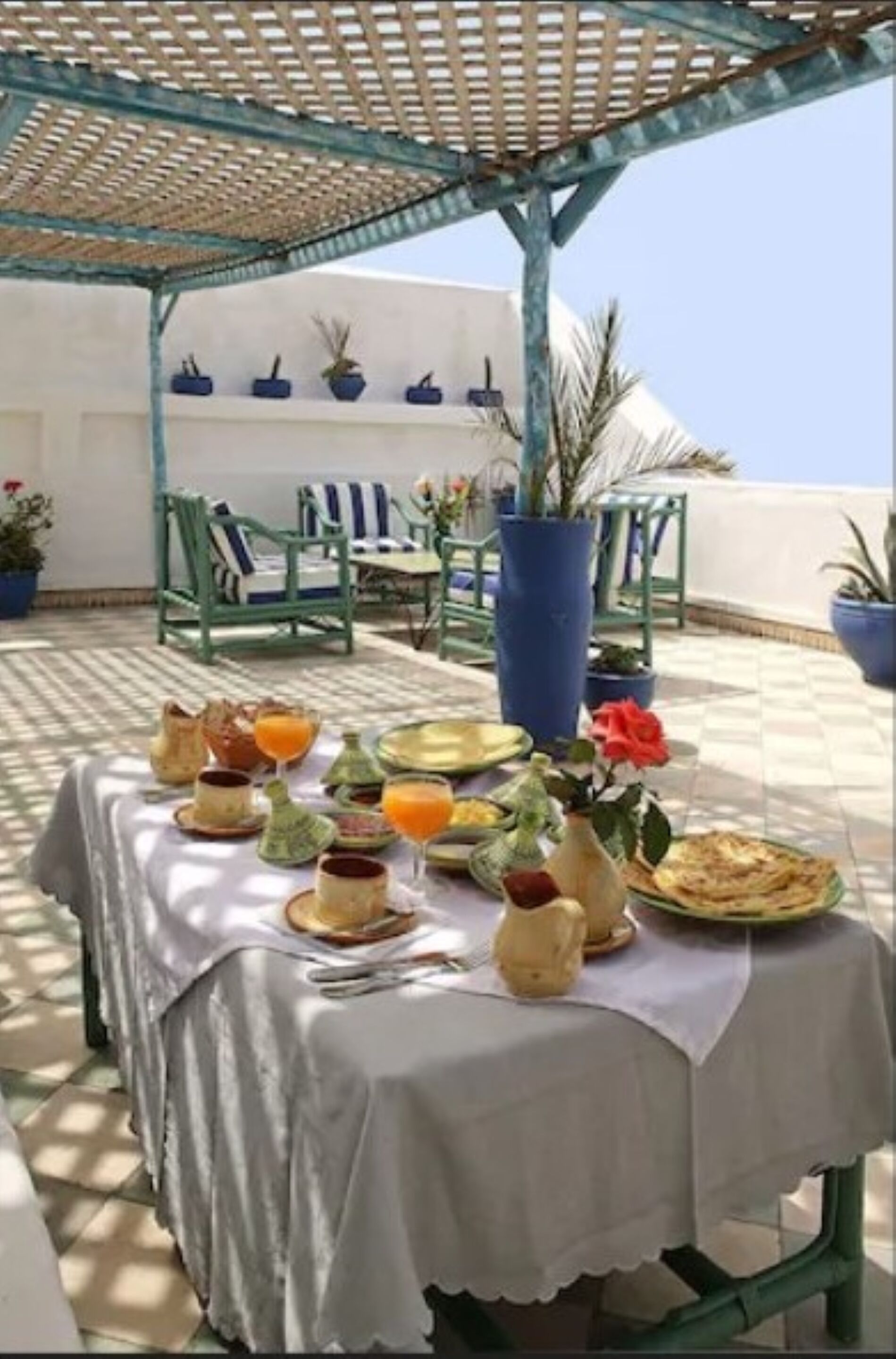 Eine Terrasse mit einem Frühstückstisch, komplett mit Tellern, Gläsern und einer Vase mit Blumen.