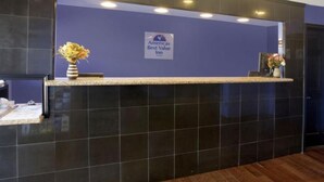 Een receptiebalie met een donkere betegelde achtergrond, een bord met 'Americas Best Value Inn' en een bloemenvaas op de balie.