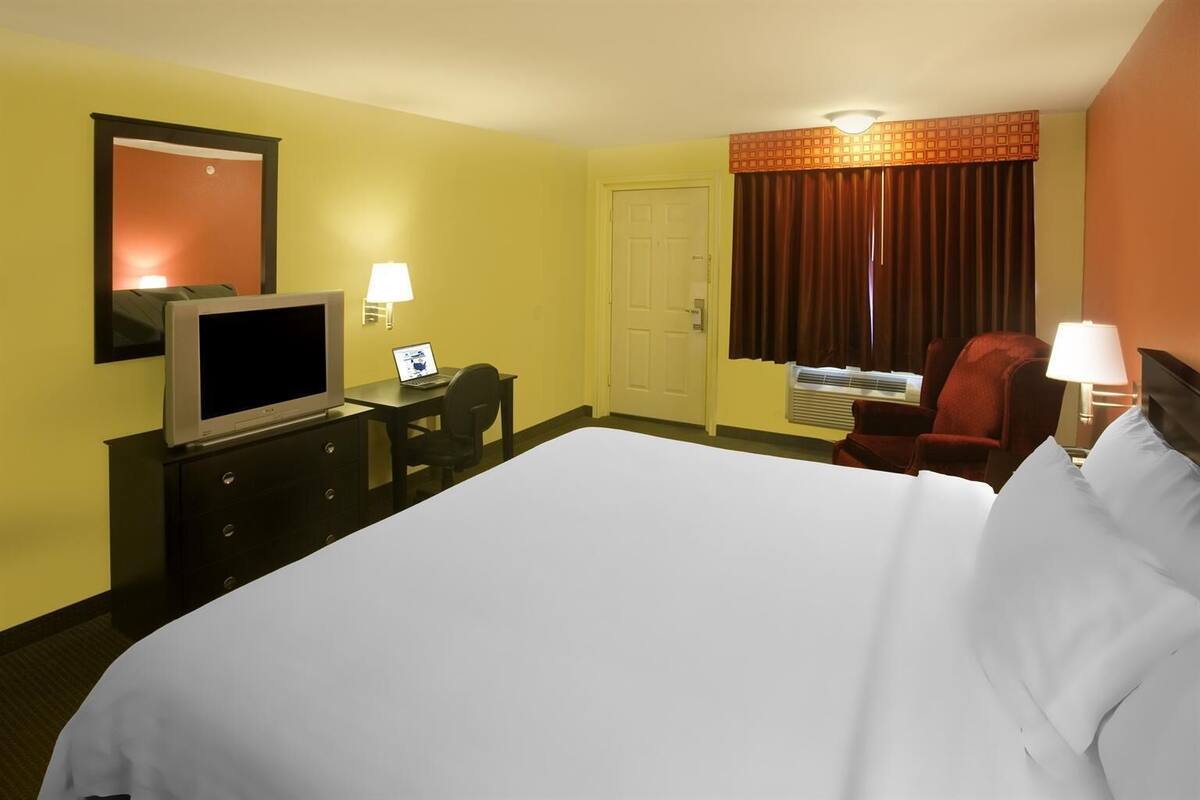 A hotel room with a large bed, a desk with a computer, a television, and a chair.
