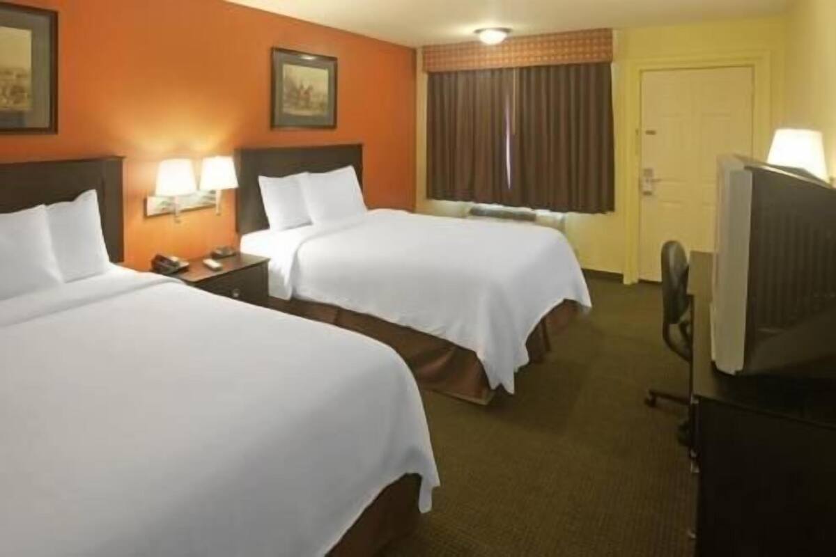 A hotel room with two beds, a television, and a window with curtains.