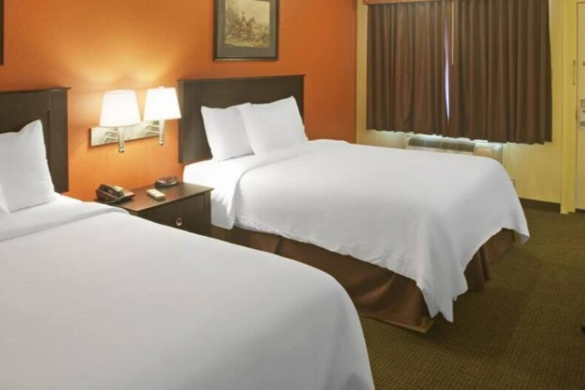 A hotel room with two beds, a desk with a lamp, a television, and a door.