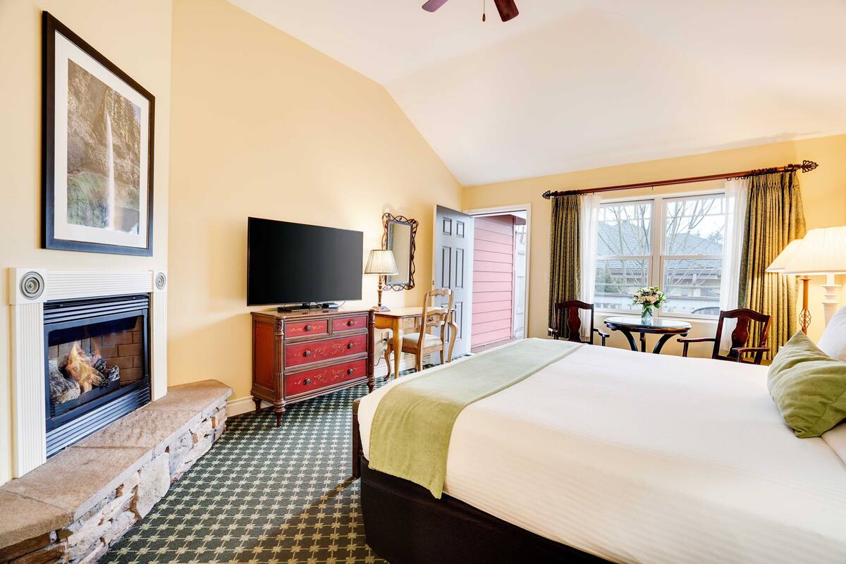 A hotel room with a fireplace, a bed, a television, a desk, and a window with curtains.