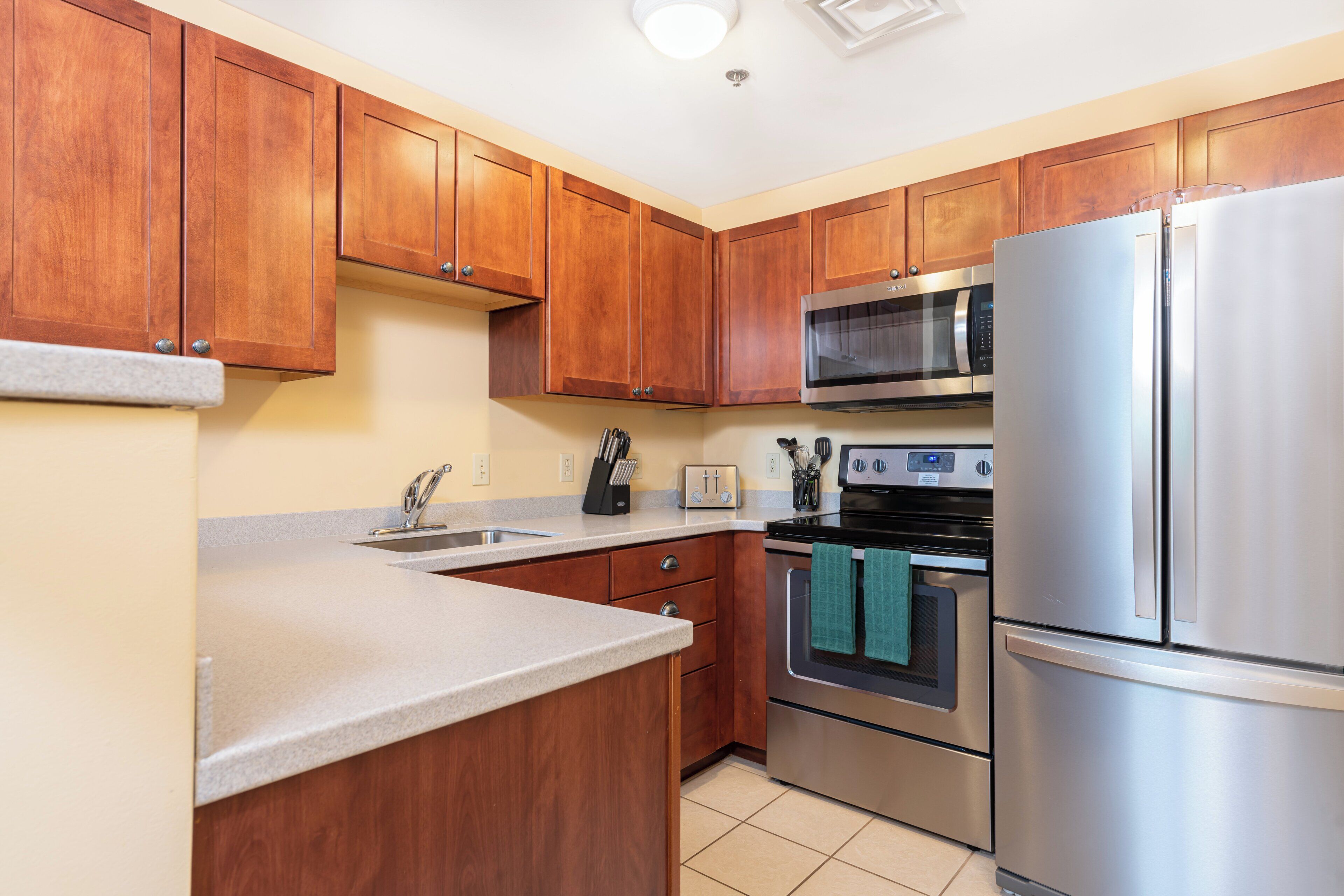 A modern kitchen with wooden cabinets, stainless steel appliances, a microwave, oven, and a refrigerator.