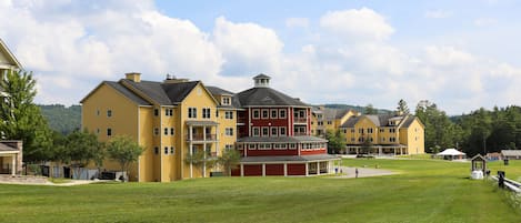A large, multi-story building with a central red section and yellow wings, surrounded by a grassy area and trees.