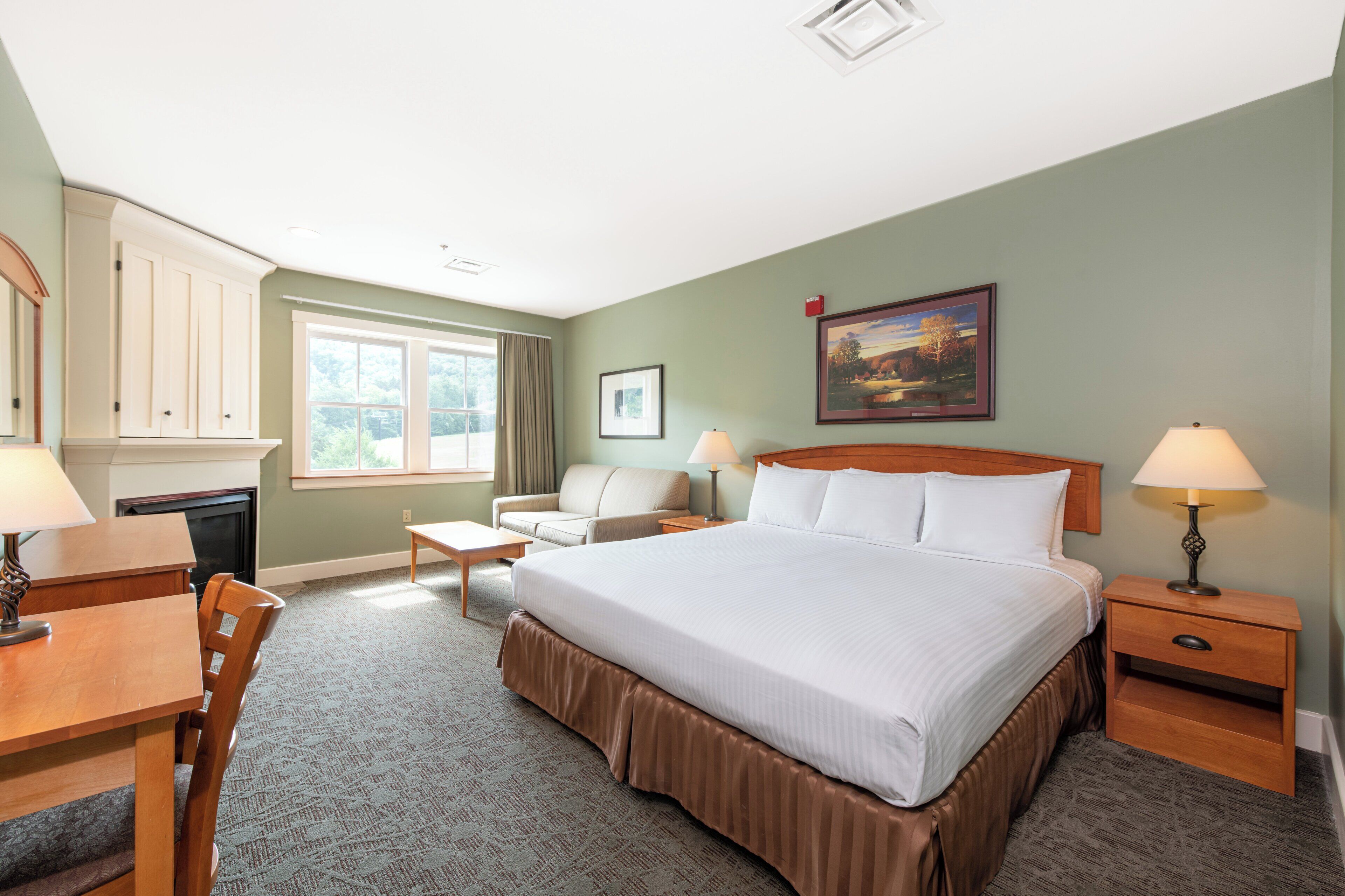 A hotel room with a large bed, a desk, a chair, a sofa, a nightstand, and a lamp.