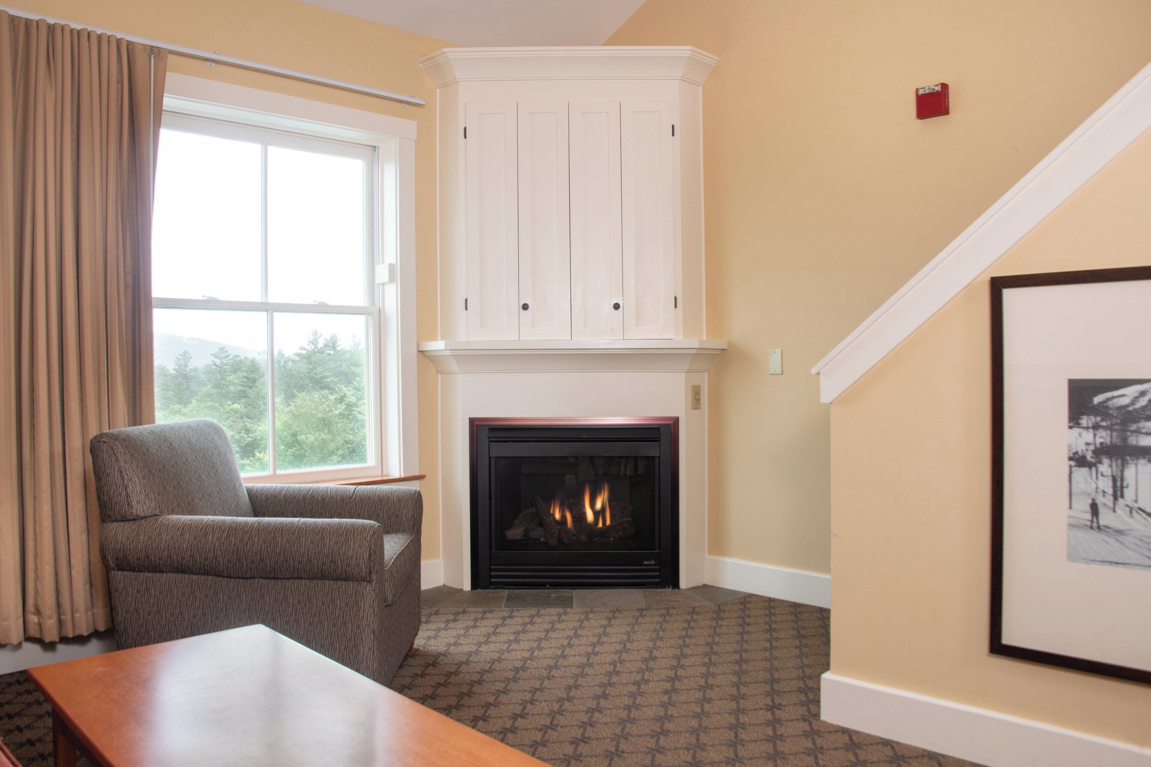 A living room with a fireplace, a large window with curtains, a sofa, and a framed picture on the wall.