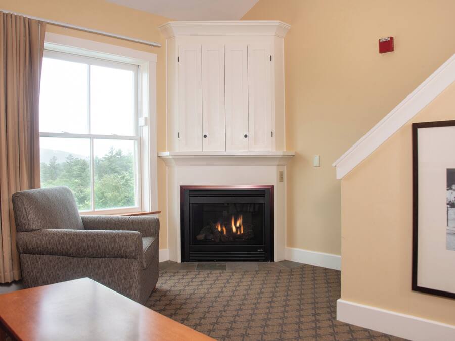 A living room with a fireplace, a large window with curtains, a sofa, and a framed picture on the wall.